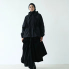 Person wearing a black hooded parka by Rashawl with a hijab against a white background