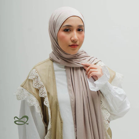 A woman wearing a beige-colored oval-edge pashmina scarf, paired with a lace-trimmed top.