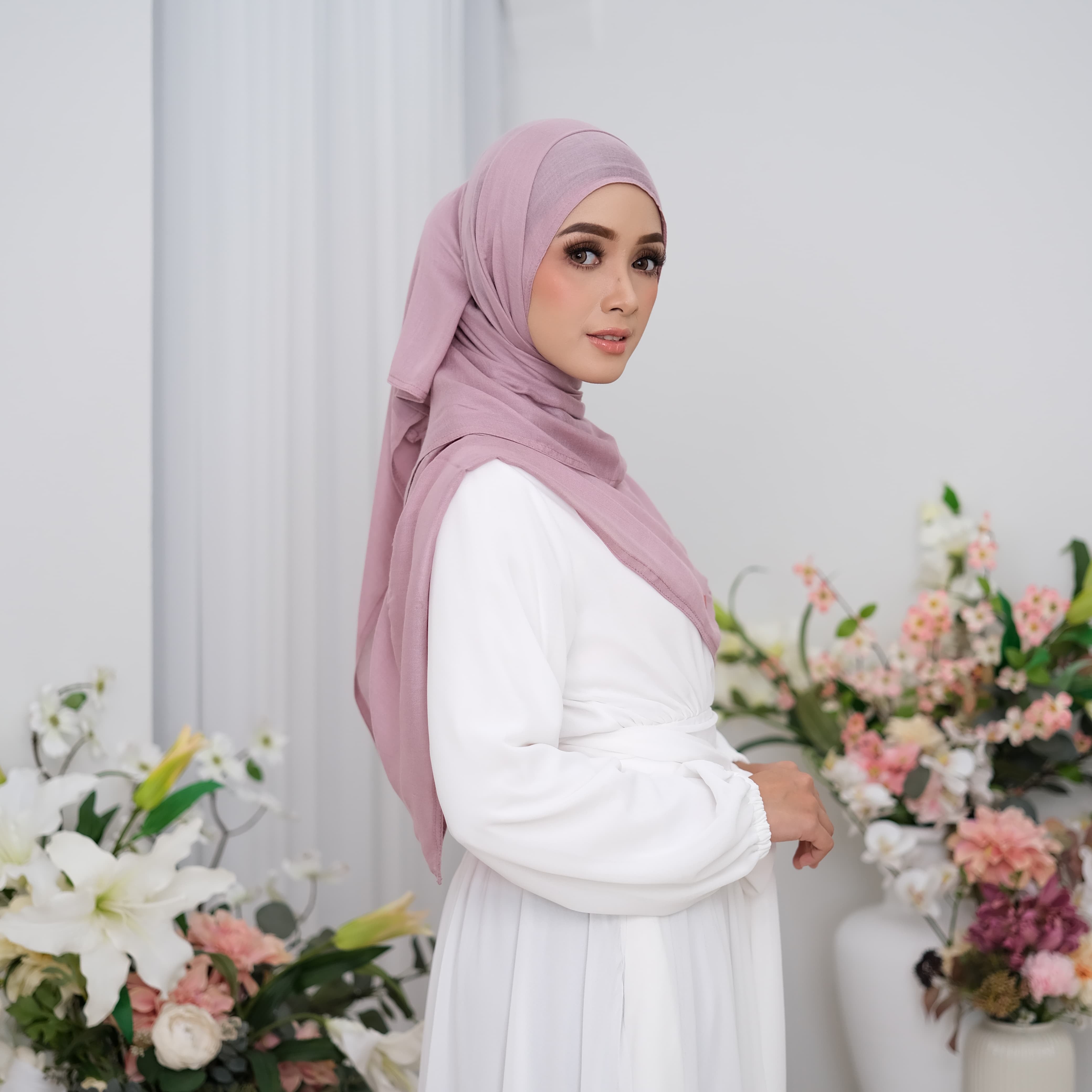 Woman wearing a pink hijab pashmina viscose and white outfit with floral decorations in the background