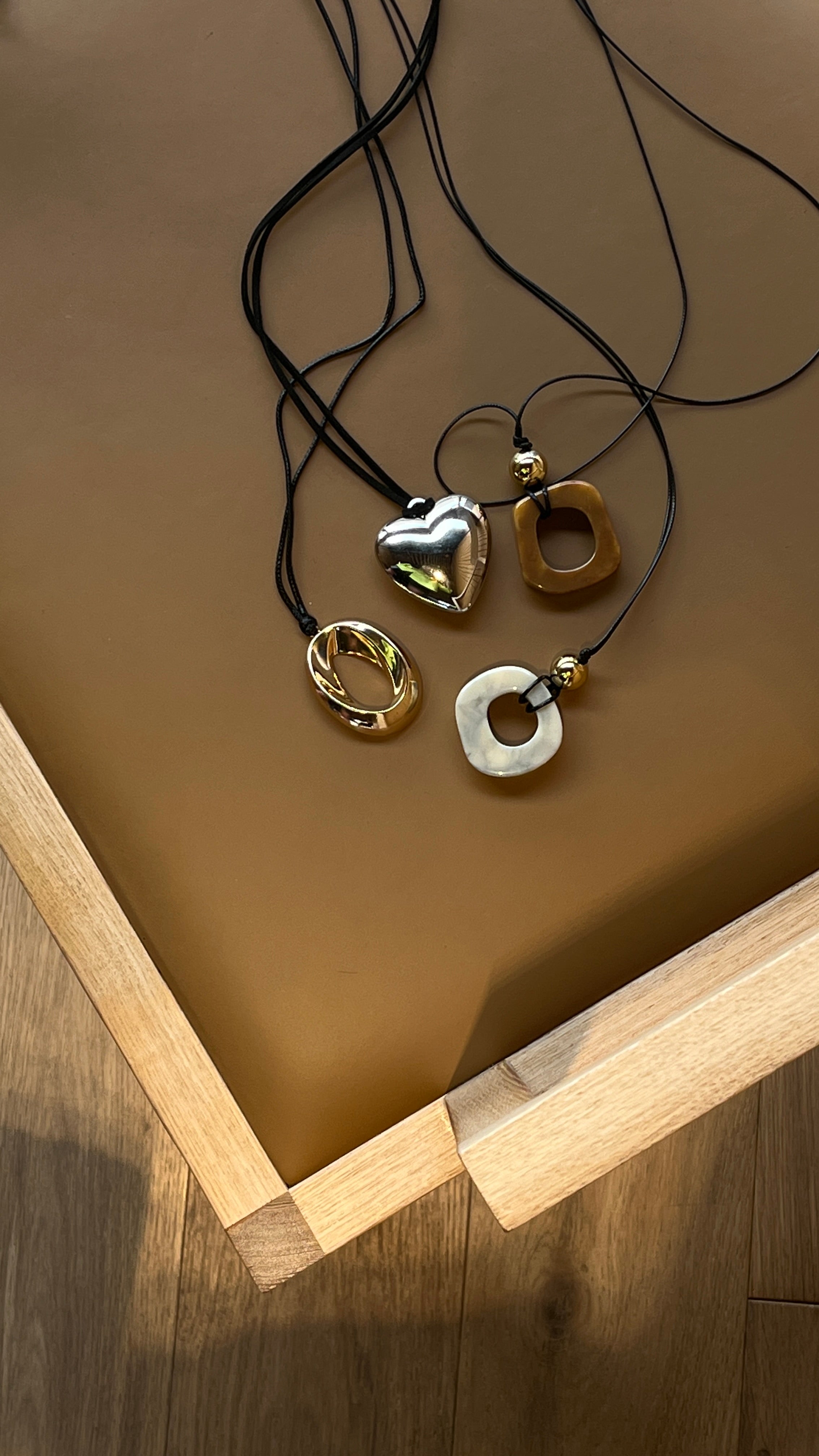 Four necklaces by Darje with different pendants on a brown surface