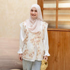 Woman wearing a floral vest by Haidee Orlin over white shirt and hijab standing indoors with a wooden panel background
