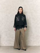 Woman wearing a black shirt with lace details by Studio Tui and beige pants against a neutral background