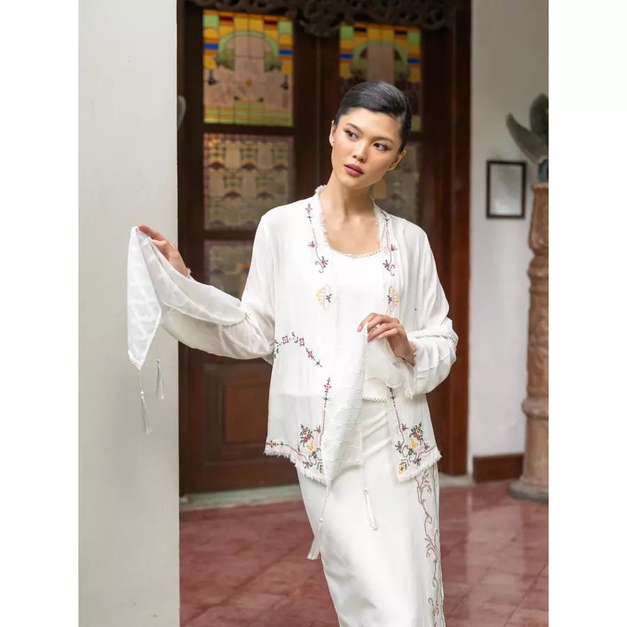 Woman wearing a traditional white kebaya and prana shawl by Kartinis Label with floral embroidery in an indoor setting.