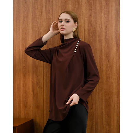 Woman wearing a brown Rachel Blouse by Kasa Heritage with pearl details against a wooden background