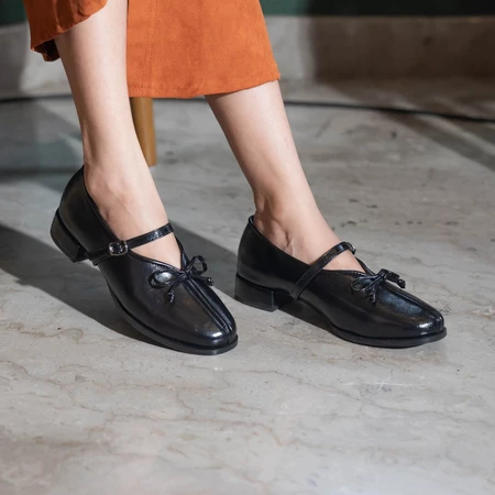 A person wearing black, pointed, flat shoes with a buckle strap across the foot by Dianable.