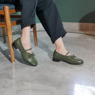 A person wearing green, pointed, flat shoes with a buckle strap across the foot by Dianable.