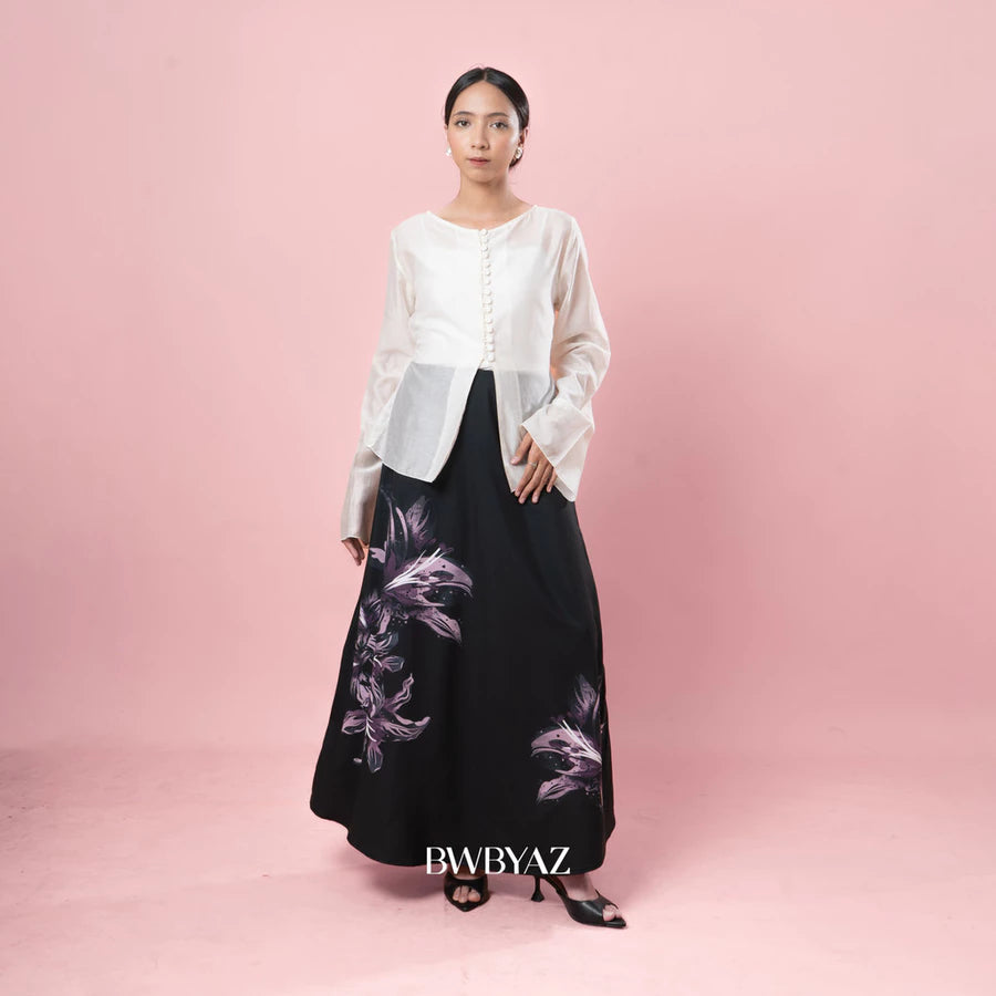 Woman wearing a white top and black skirt with floral design on a pink background, featuring the brand BWBYAZ.