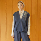 Person wearing a blue embroidered vest by Jenna & Kaia over a white shirt against a wooden background