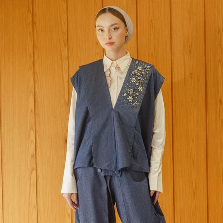 Person wearing a blue embroidered vest by Jenna & Kaia over a white shirt against a wooden background