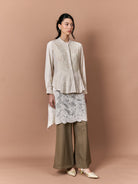 Woman wearing a beige embroidered  shirt by Studio Tui, lace skirt, and brown pants against a beige background
