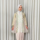 Woman wearing a patterned kebaya by Kartinis Label and hijab against a plain background