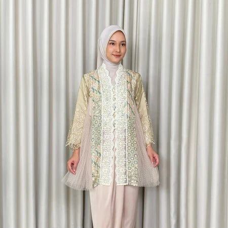 Woman wearing a patterned kebaya by Kartinis Label and hijab against a plain background