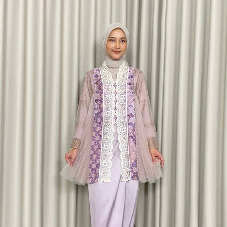 A woman wearing a traditional Kebaya Heather dress by Kartinis Label with batik and lace decorations, featuring a silhouette commonly associated with casual to elegant attire.