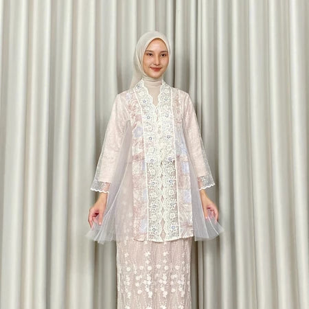 A woman modeling a white Kartinis Label kebaya, featuring batik and lace details, with a silhouette of a traditional kebaya dress.