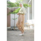 A woman standing in an outdoor setting wearing beige pants by Abame and a matching top.