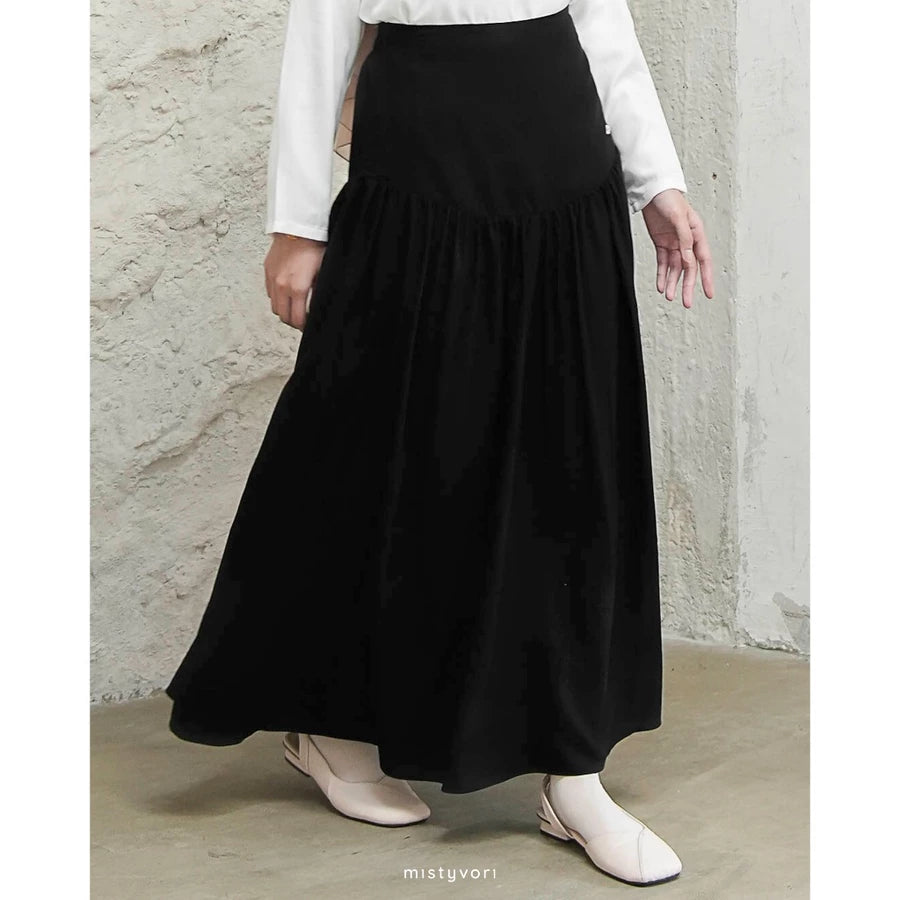 Person wearing a black skirt by Mistyvori and white top against a concrete wall.