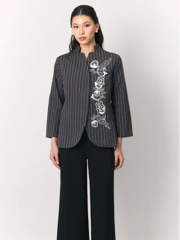 A woman modeling a black three-quarter sleeve top by Studio Tui with vertical red and white stripes and white floral embroidery on the front, paired with black wide-leg trousers, against a light gray studio background.