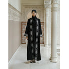 Woman in a black abaya with white embroidery by Tubita standing in an ornate hallway.
