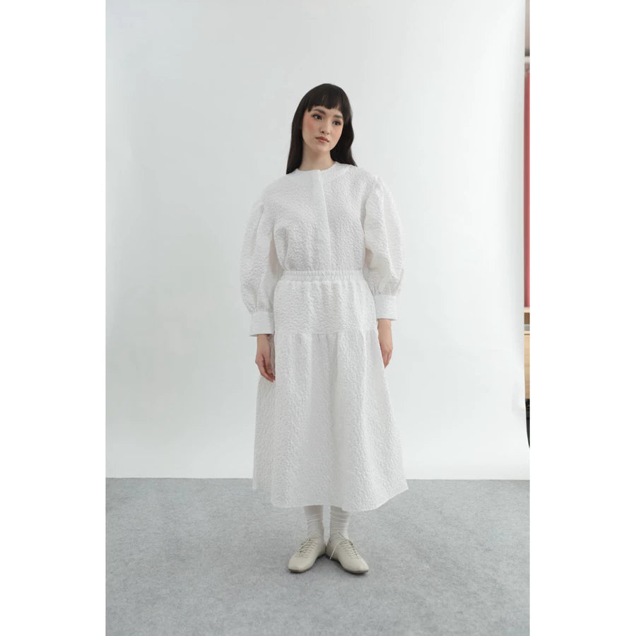 Person wearing a white top and patterned long white skirt by Yestoday on a gray background