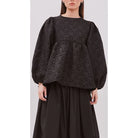 Person wearing a dark embossed peplum dress by Yestoday with puffed sleeves on a plain background