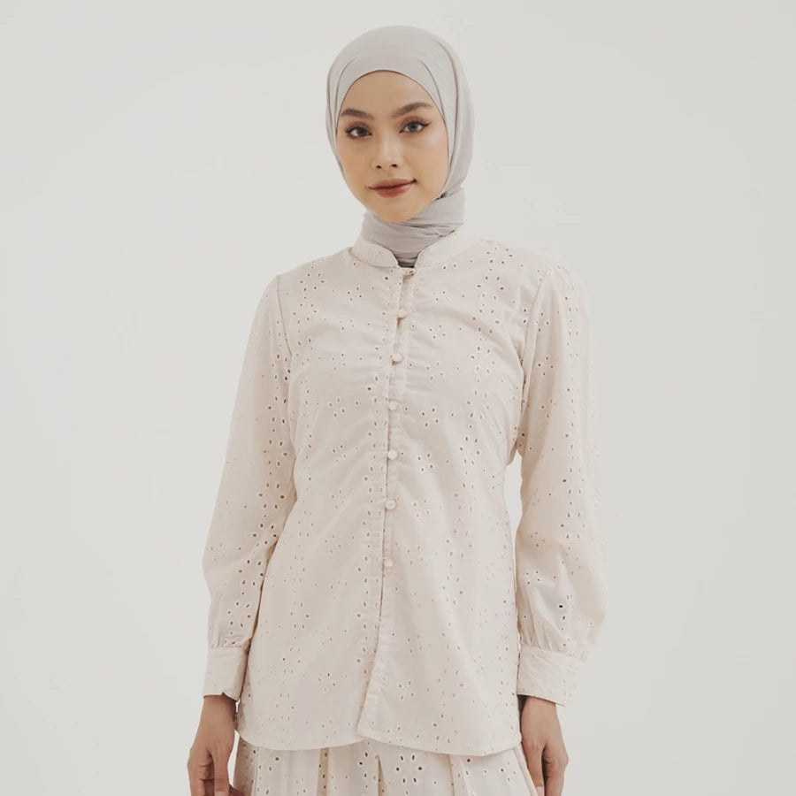 Woman wearing a light-colored blouse by Tunique with intricate patterns on a plain background