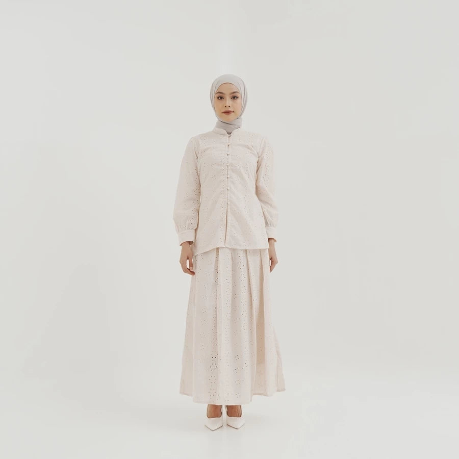 Person wearing a light-colored patterened skirt by Tunique with a hijab on a white background
