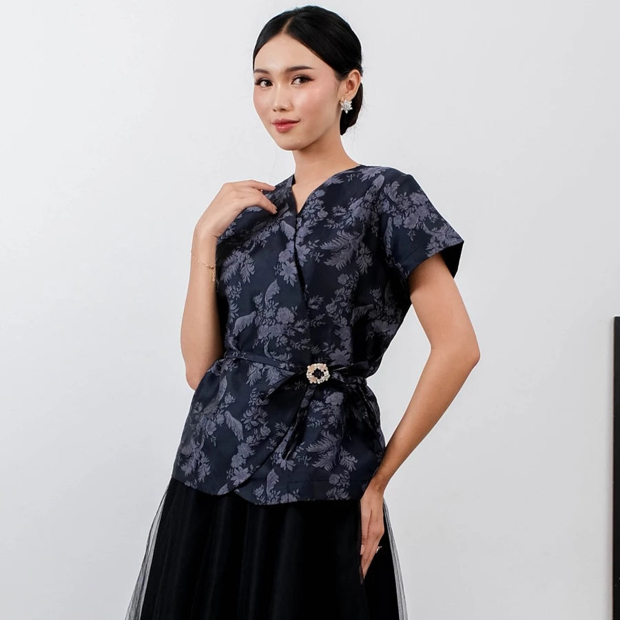 Woman wearing a navy floral blouse by Holy Peony with a belt against a white background
