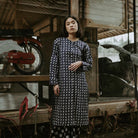 A woman wearing a long-sleeved navy blue tunic with a white geometric pattern, standing in a rustic wooden structure with a red motorcycle in the background.