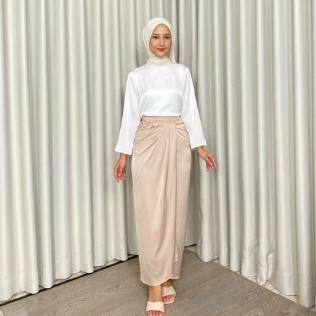 Woman wearing a white top and beige skirt by Kartinis Label against a white curtain background