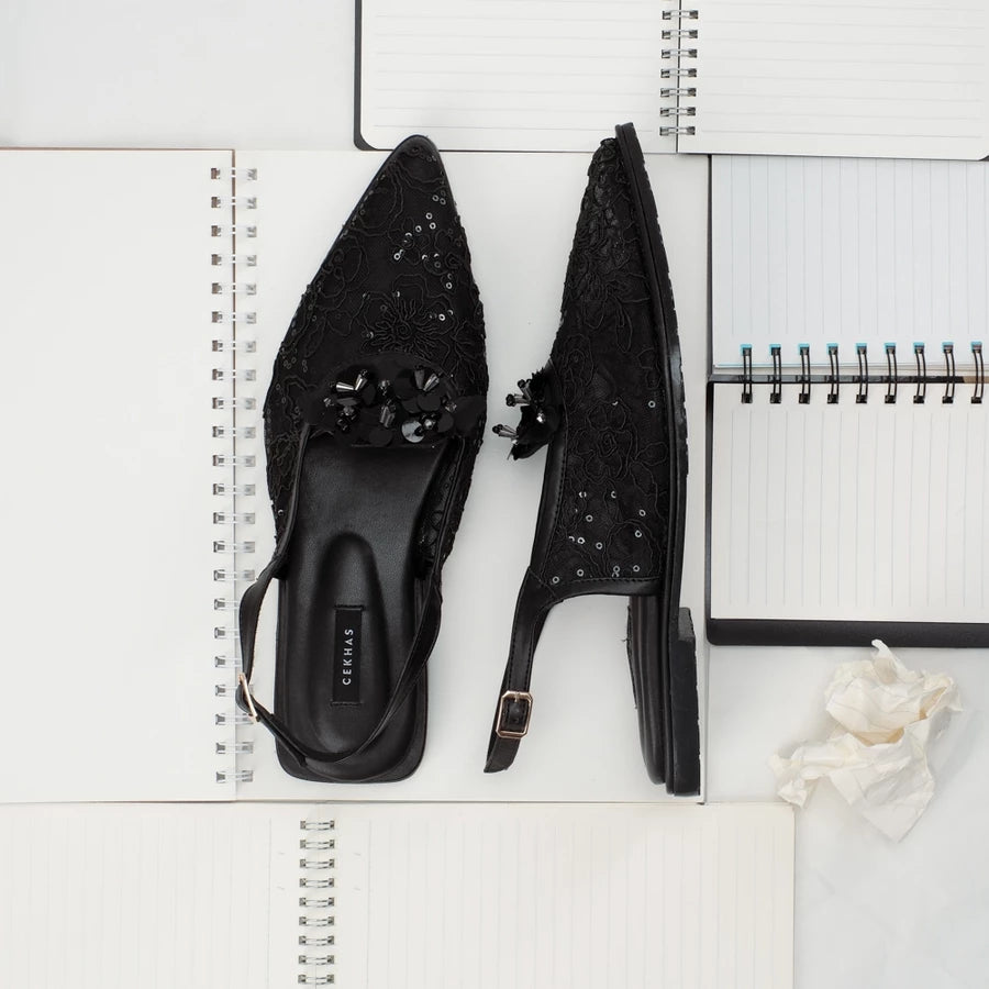 Black studded sandals by Cekhas on a white surface with a notebook and flower.
