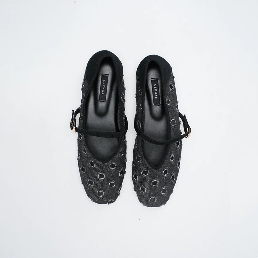 A pair of black Mary Jane flatshoes with a textured, woven geometric pattern and black straps, shown from a top-down view on a white background.