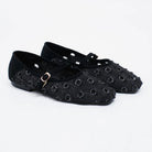 A pair of black flatshoes with a textured, woven circular pattern and a small gold buckle on the strap by Cekhas, shown on a white background.