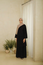 Woman wearing a long black tunic with wide sleeves and front button details, paired with a black maxi skirt and light brown hijab for an elegant minimalist look.

Wanita mengenakan tunik panjang warna hitam berlengan lebar dan detail kancing depan, dipadukan dengan rok panjang hitam serta hijab berwarna coklat muda untuk tampilan anggun dan minimalis.