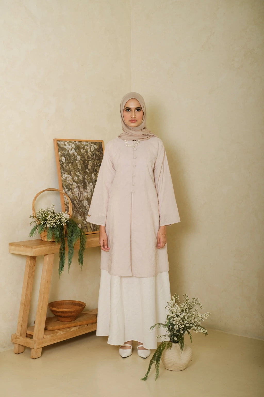 Woman wearing a long beige tunic with wide sleeves and front button details, paired with a white maxi skirt and matching hijab for an elegant minimalist look.

Wanita mengenakan tunik panjang warna beige berlengan lebar dan detail kancing depan, dipadukan dengan rok panjang putih serta hijab senada untuk tampilan anggun dan minimalis.