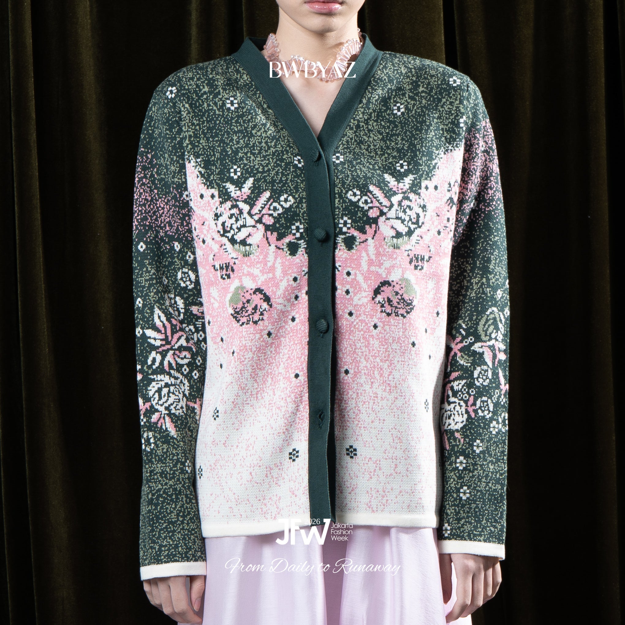 Person wearing a green cardigan with pink and white floral pattern by BWBYAZ with a dark background