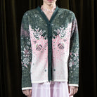 Person wearing a green cardigan with pink and white floral pattern by BWBYAZ with a dark background