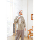 A woman wearing an olive green shirt by Abame with a long sleeves, paired with light brown trousers, standing in a room with a light decor.