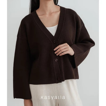 Person wearing a dark brown cardigan over a white shirt with a plain background, featuring the brand 'kasyalia'.