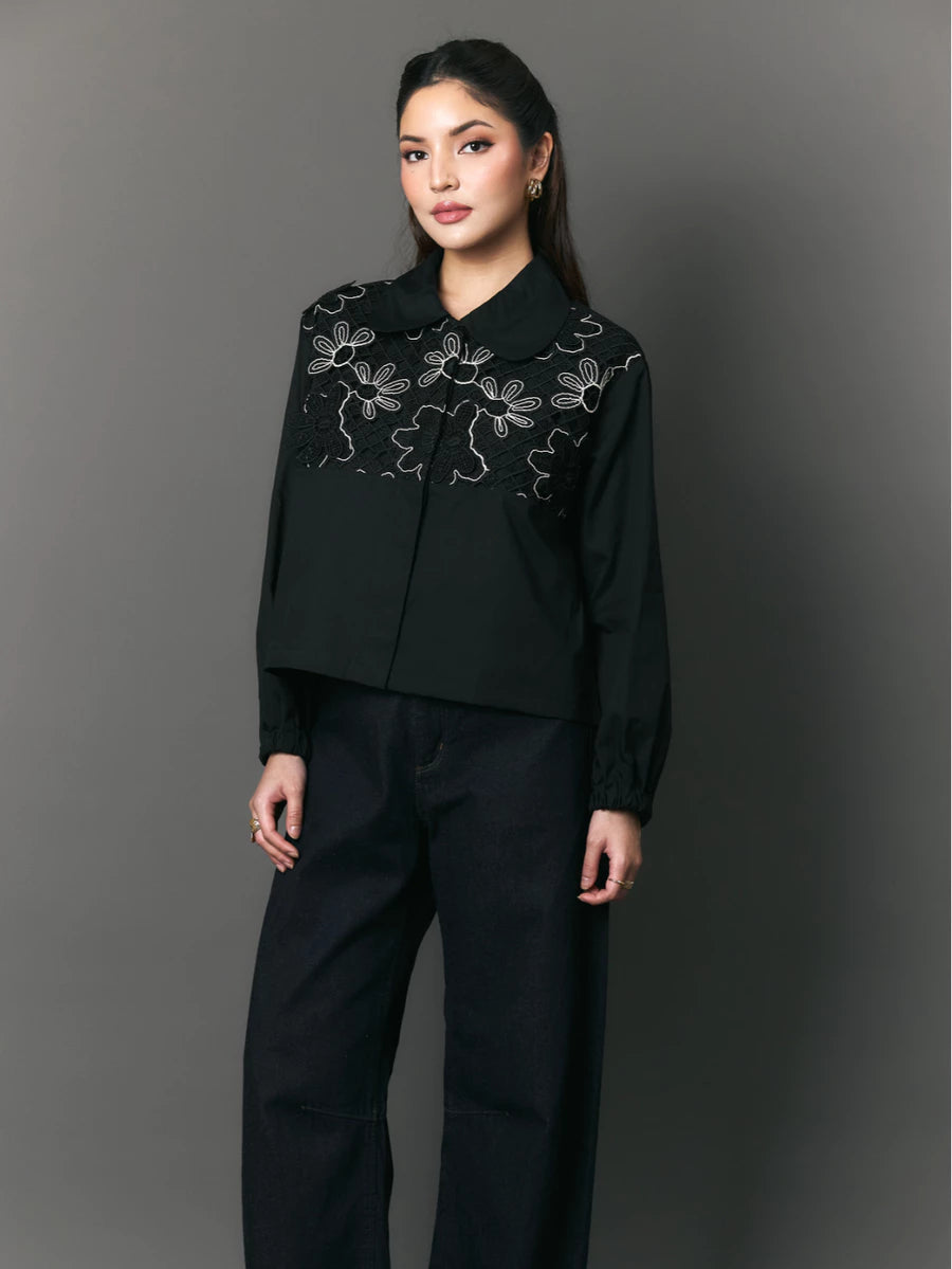 Woman wearing a black shirt with floral embroidery by Studio Tui against a gray background