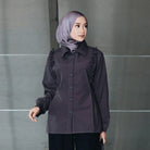 Woman wearing a dark brown blouse with ruffled sleeves from Atala Scarves against a gray wall