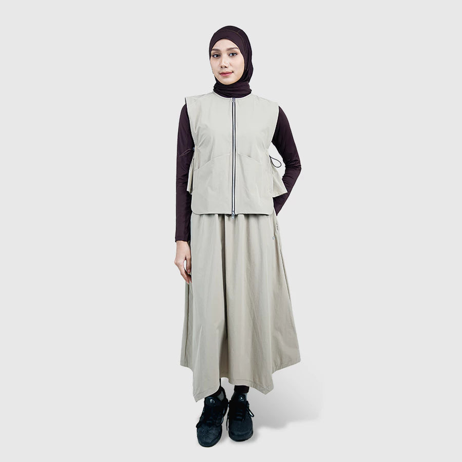 Person wearing a beige vest by HIA and long skirt with a black hijab on a white background