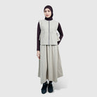 Person wearing a beige vest by HIA and long skirt with a black hijab on a white background