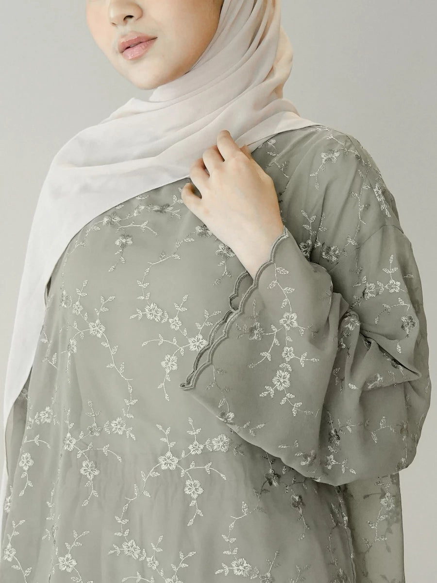 Person wearing a light green floral blouse by Mistyvori with a white hijab on a plain background