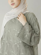 Person wearing a light green floral blouse by Mistyvori with a white hijab on a plain background