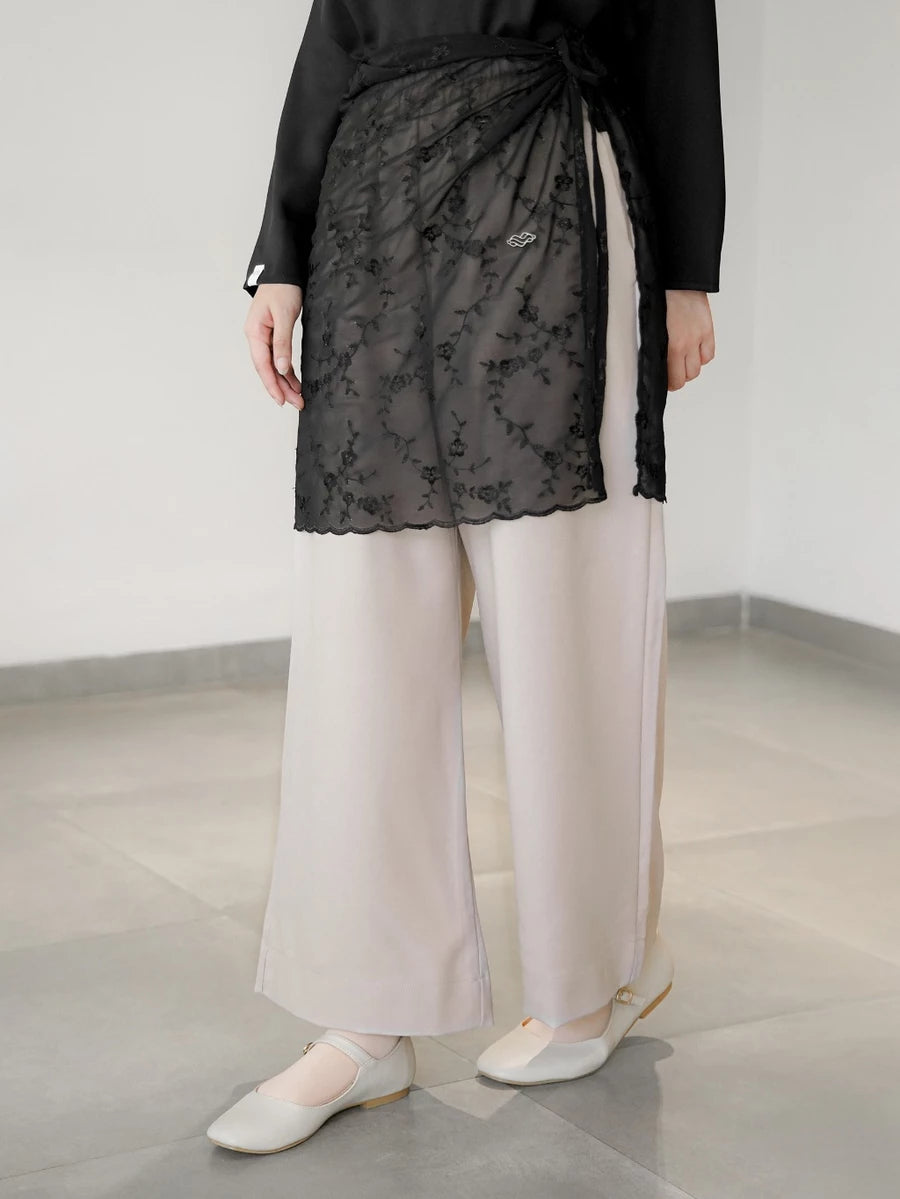 Person wearing a black top, lace layered skirt by Mistyvori, and light-colored pants in a minimal indoor setting