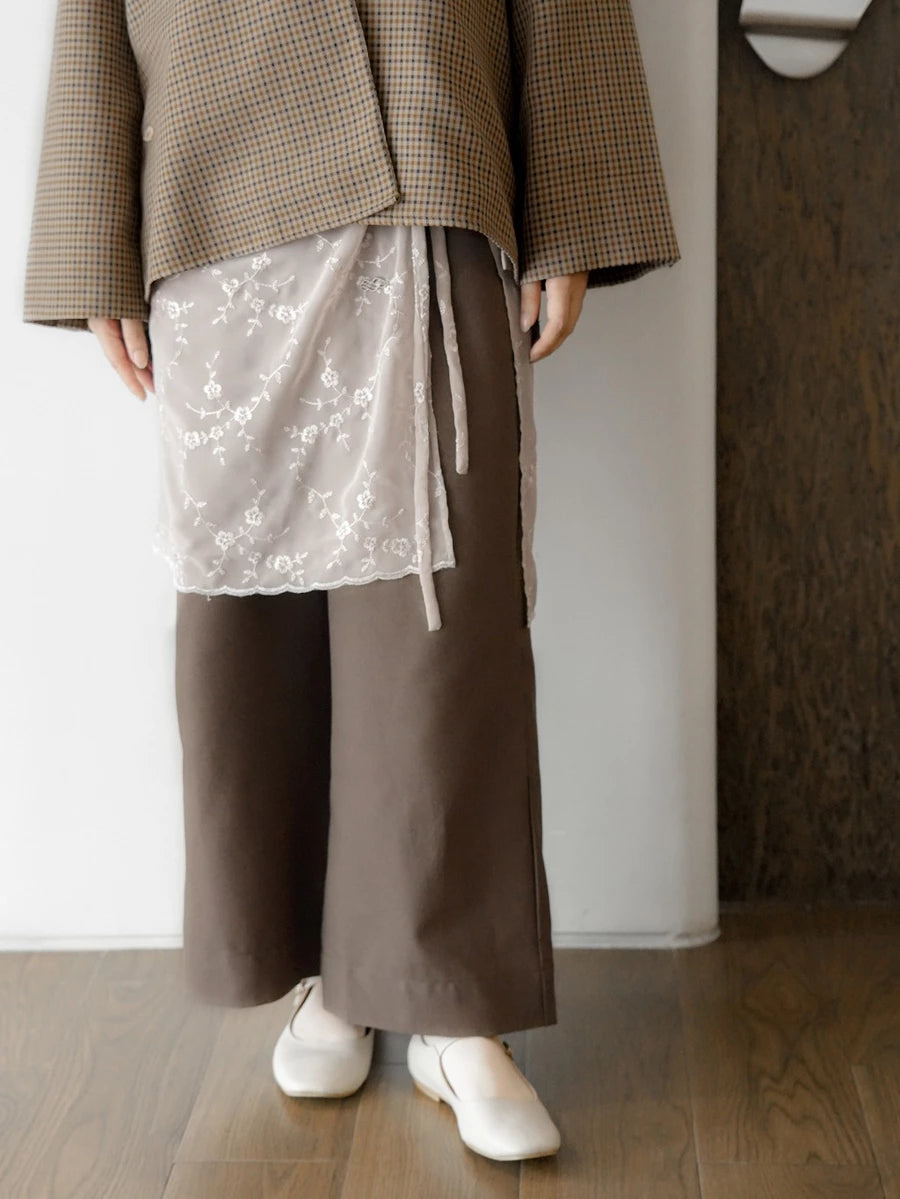 Person wearing a brown coat, broken white floral layered skirt by Mistyvori, and brown wide-leg pants indoors.