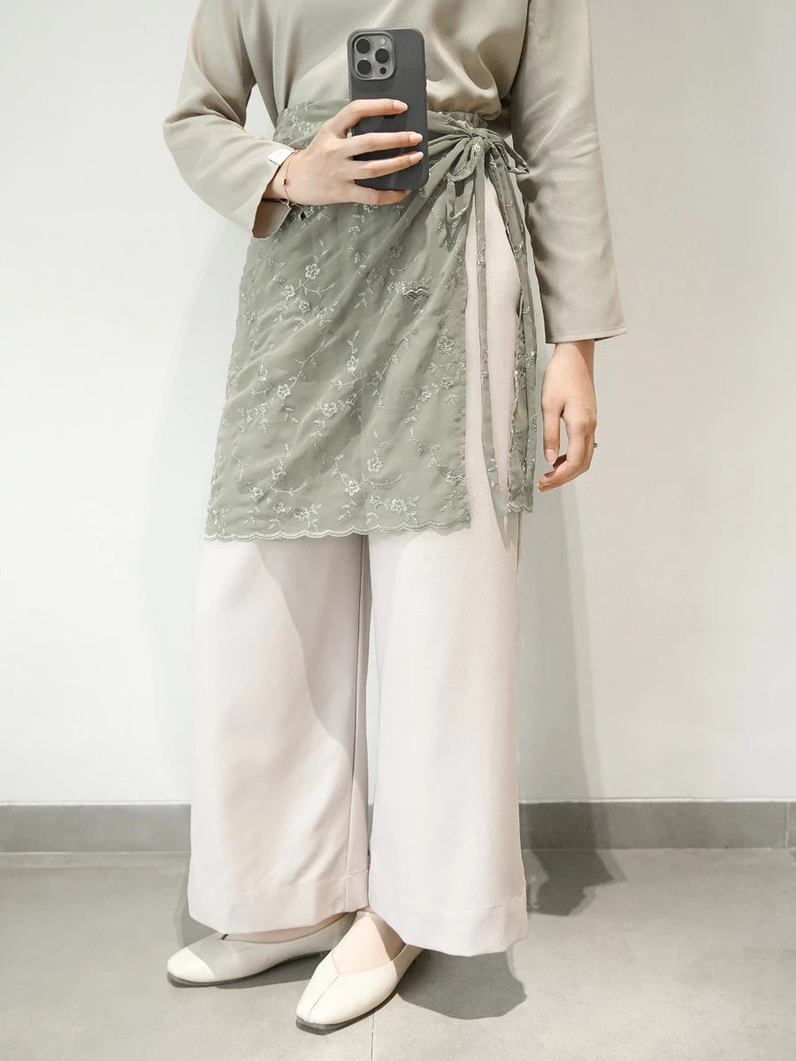 Person wearing a light green top, light green lace layered skirt by Mistyvori, and white pants against a plain background