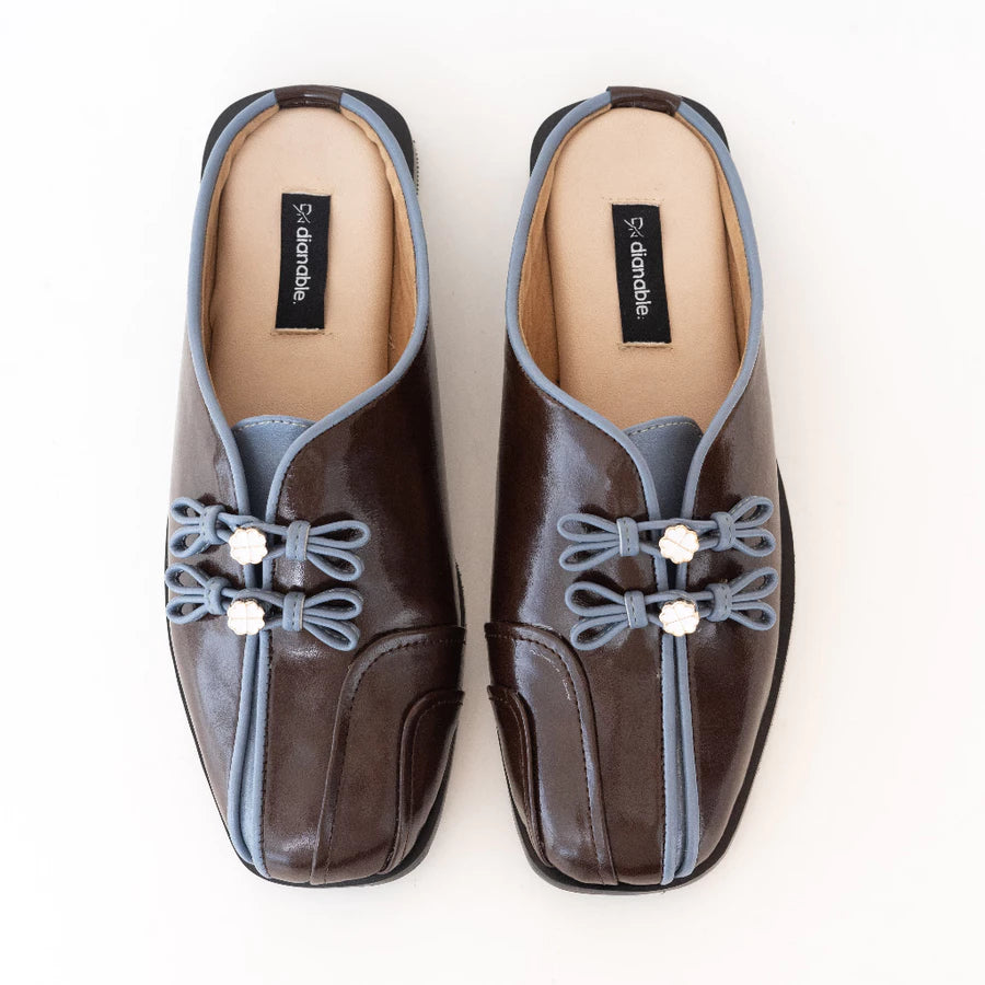 Pair of brown mules flats by Dianable with decorative elements on a white background
