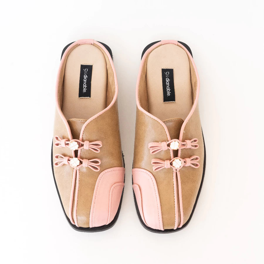 Pair of tan and pink mules flats by Dianable with decorative bows on a white background
