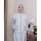 Woman in a white and light gray shirt by Abame standing indoors with a neutral background